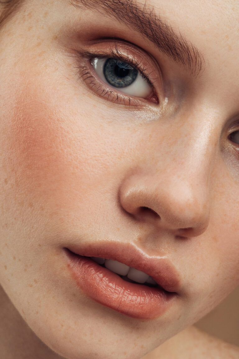 Natural beauty is highlighted in this close-up image of a young woman, showcasing her clean skin, subtle makeup, and glowing complexion. The intimate framing emphasizes the small details, from distinct freckles to smooth texture, creating a fresh and authentic feel.